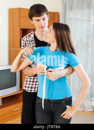 Guy measuring bust of girl with measuring tape at home Stock Photo