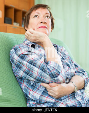 Stressed woman pensioner laying on her elbows and thinking indoor Stock Photo