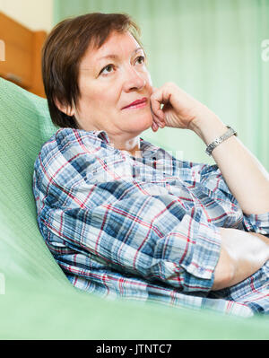 Thoughtful woman with sad face and in casual clothes laying on sofa Stock Photo