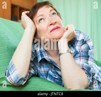 Stressed elderly woman laying on her elbows and thinking  on couch Stock Photo