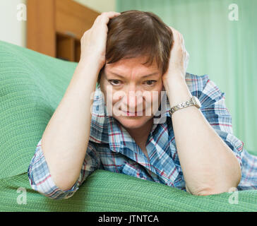 Thoughtful senior woman with sad face and in casual clothes laying on sofa Stock Photo