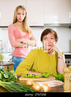 adult daughter and senior mother after quarrel in kitchen Stock Photo
