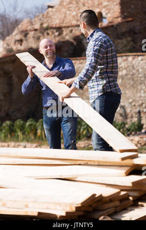 Two adult male builders carrying over plane boards at site Stock Photo