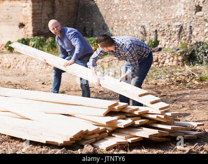 Two smiling male builders carrying over plane boards at site Stock Photo