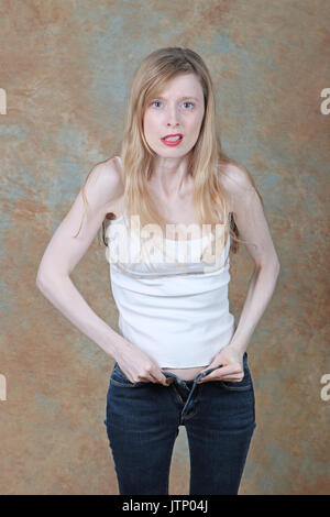 Young slim girl struggling to zip up tight skinny jeans showing frustration on her face