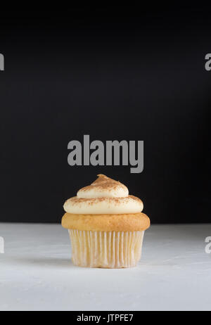 Cup cake background with single cupcake on white topped with cinnamon custard on rustic white with defocused black background - space for text Stock Photo