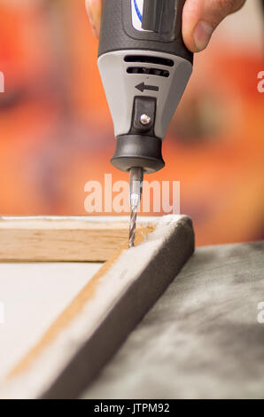 Closeup of a hardworker man drilling a wooden frame with his drill over a gray table in a blurred background Stock Photo