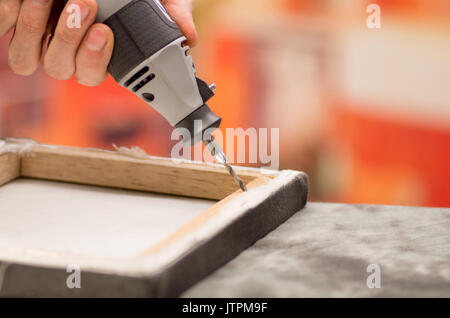 Closeup of a hardworker man drilling a wooden frame with his drill over a gray table in a blurred background Stock Photo