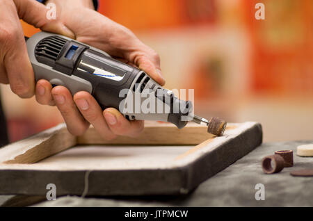 Closeup of a hardworker man using a polisher in a wooden frame, on a gray table in a blurred background Stock Photo