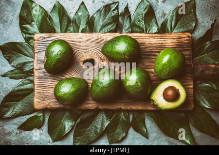 food background with fresh avocado, avocado tree leaves and wooden cutting board. Harvest concept, Guacamole ingredients. Healthy fat, omega 3. Half o