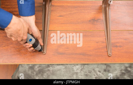 Closeup of a hardworker man drilling a a metallic piece in a wooden piece with his drill, in a gray background, top view Stock Photo