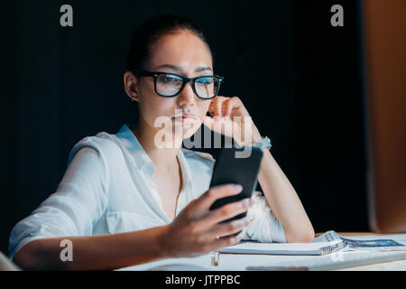 young tired asian businesswoman in eyeglasses using smartphone and working till late in office Stock Photo