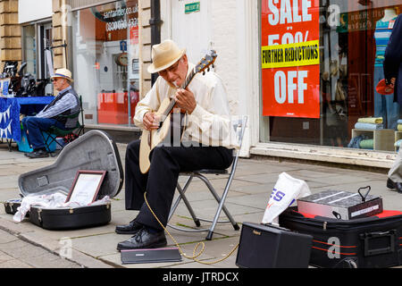 Melton Mowbray folk festival and craft fair, senior street musician sitting playing the guitar outside Santander bank alongside a market trader Stock Photo