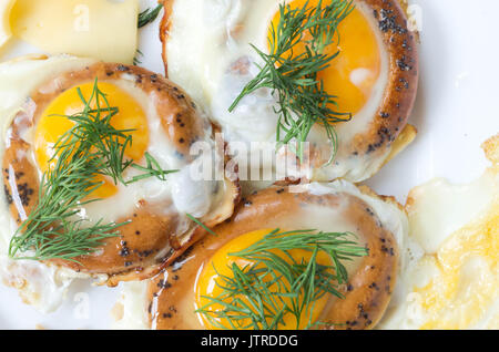 Three fried eggs. Eggs fried in bread. Yolks and greens. Stock Photo
