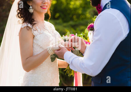 Groom wears ring on bride's finger. Newlyweds exchange rings on registration of marriage in the open air. Close-up of man putting a ring on womans fin Stock Photo