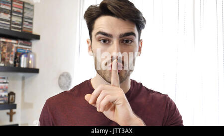 Handsome young man doing Hush sign with finger on lips Stock Photo