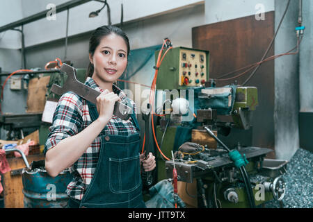 smiling lathe factory worker looking at camera when she ready to using large wrenches repair working milling machine device. Stock Photo