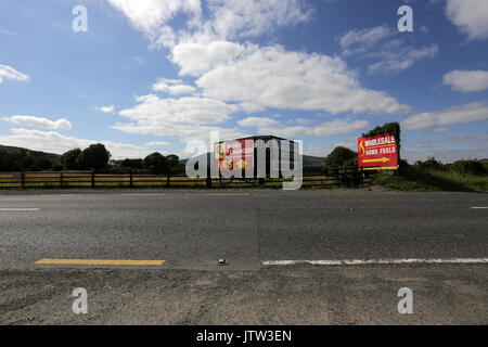 Newry, Northern Ireland. 10th August 2017. A sign for exchanging euro and sterling currencies is seen right on the border between the Republic of Ireland and Northern Ireland just outside Newry, Co Down. The line in the road in the centre of the frame is where the border occurs. It separates the road from the Republic of Ireland on the left of the frame and the road to Northern Ireland on the right of the frame. The change can be seen in the different road markings, the Republic of Ireland mark the hard shoulder by a separated yellow line and Northern Ireland by a continuous white line. Credit Stock Photo