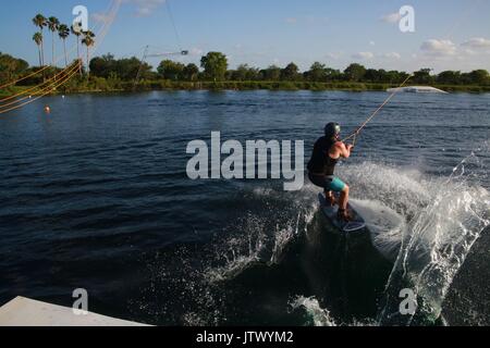 Young Woman Being Launched Pulled by Cable on Wakeboard into Lake Stock Photo