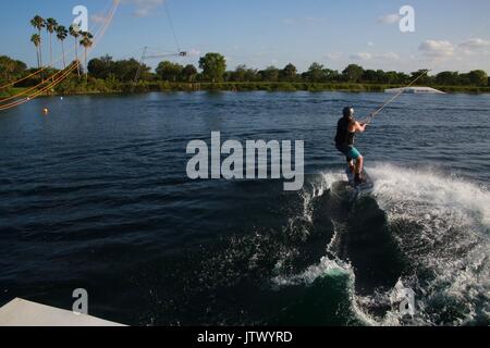 Young Woman Being Launched Pulled by Cable on Wakeboard into Lake Stock Photo