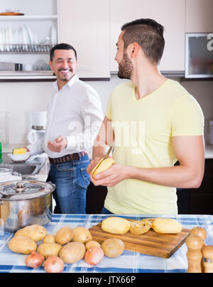 Adult son helping happy father to prepare vegetable stew at kitchen Stock Photo