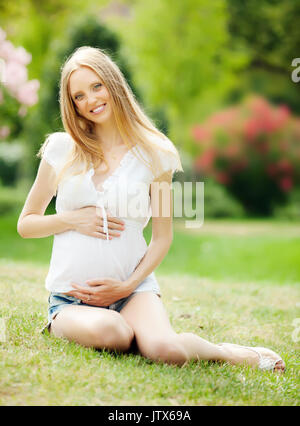 Long-haired happy pregnant woman on grass in  summer park Stock Photo