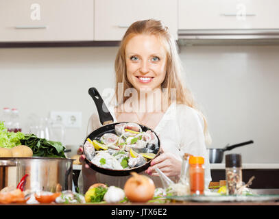 Cheeful woman cooking fish   in frying pan at  kitchen Stock Photo