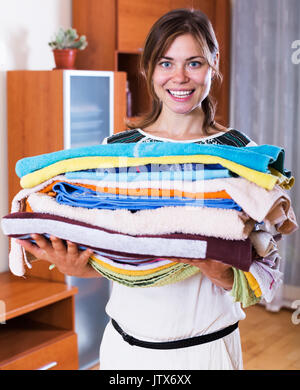 Positive woman carrying washed laundry to iron and smiling Stock Photo