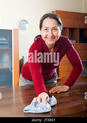 Happy mature housewife cleaning table with cleanser and rag at living room Stock Photo