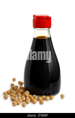 Glass bottle of soya sauce with red plastic lid isolated on white. Spilled soya beans. Stock Photo