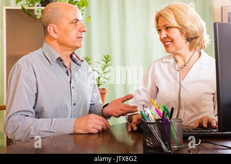 Elderly man talking with smiling female doctor in clinic office Stock Photo