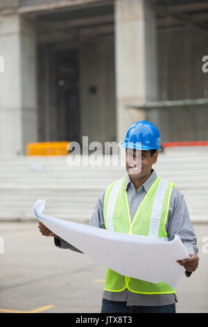 Indian construction manager or Architect checking the blueprint plans at a building site. Stock Photo