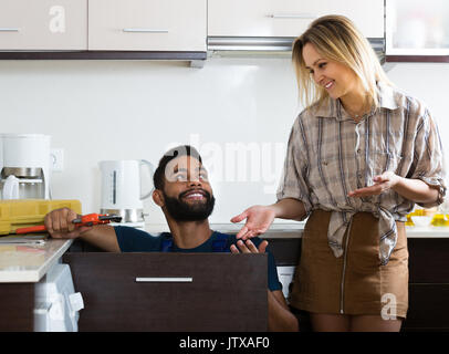 Young African plumber and smiling white housewife in domestic kitchen Stock Photo