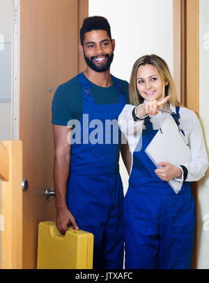 Happy handyman with assistant in uniform at apartment entrance Stock Photo