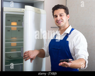 Serviceman fixing technical problems with fridge in domestic  interior Stock Photo