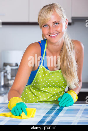 Smiling young blonde maid dusting kitchen tops Stock Photo