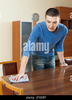 Happy man dusting wooden table with rag and cleanser at home Stock ...