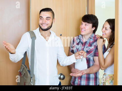 Happy couple stands with agent in the doorway looking round new apartment Stock Photo
