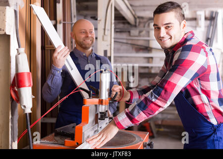 Two positive workmen working on a machine in PVC shop Stock Photo
