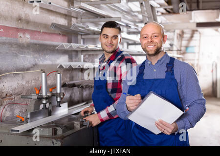 Two happy workers in coverall working with glass in factory Stock Photo