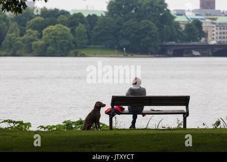 Senior man sits looking out at river, thinking, thoughtful, contemplating with his dog by his side Stock Photo