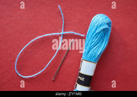 closeup of one needle, thread and skein of blue yarn on red background Stock Photo