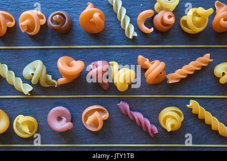 three rows of different kinds of pasta divided by thin long spaghetti on black slate background. like food shelf Stock Photo