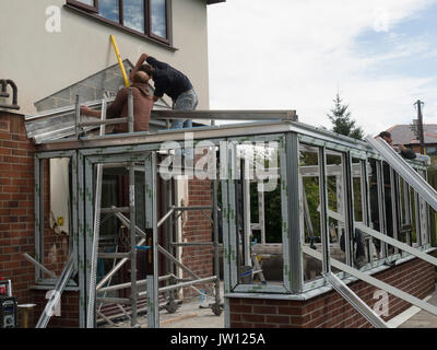 Two workmen putting the lead flashing on roof of a new conservatory another man fitting roof frame UK Stock Photo