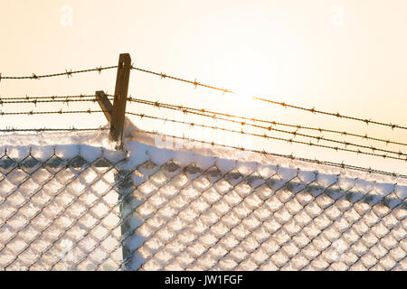 Barbed wire fence with snow at sunset. Stock Photo