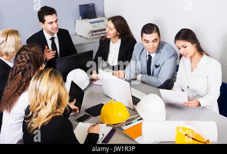 Team of positive professionals discussing business project and smiling in office. Focus on right man Stock Photo
