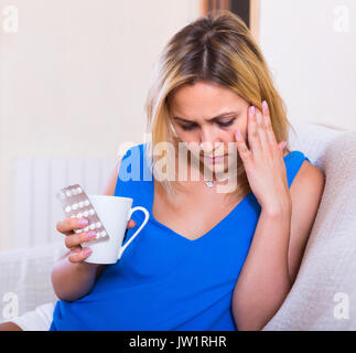 Portrait of young blonde woman suffering from heavy headache at home Stock Photo