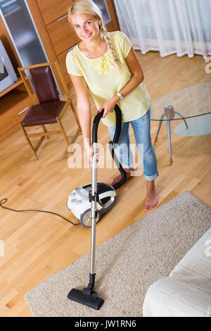 Young woman using vacuum cleaner during regular clean-up indoors Stock Photo