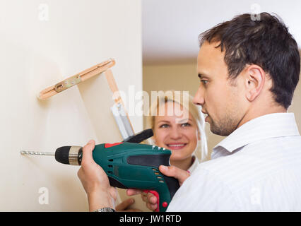 young happy couple hangs bookshelf on a wall Stock Photo