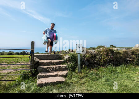 A man carrying surfboards while climbing stone steps, after returning from Gwynver Beach, Sennen, near Penzance, Cornwall, England, UK. Stock Photo